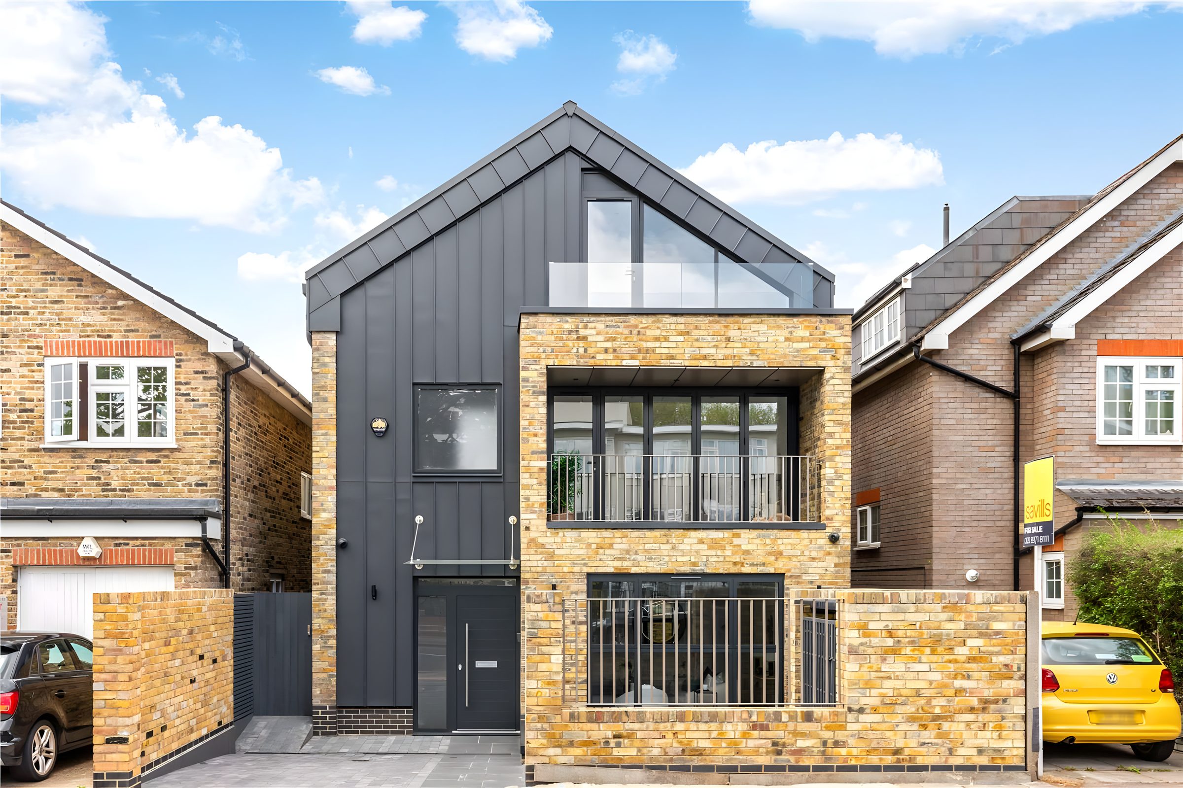 Front of the new house at 50 Woodside, with dark standing-seam zinc, yellow stock brick and a glazed gable balcony, between neighbouring homes in Wimbledon
