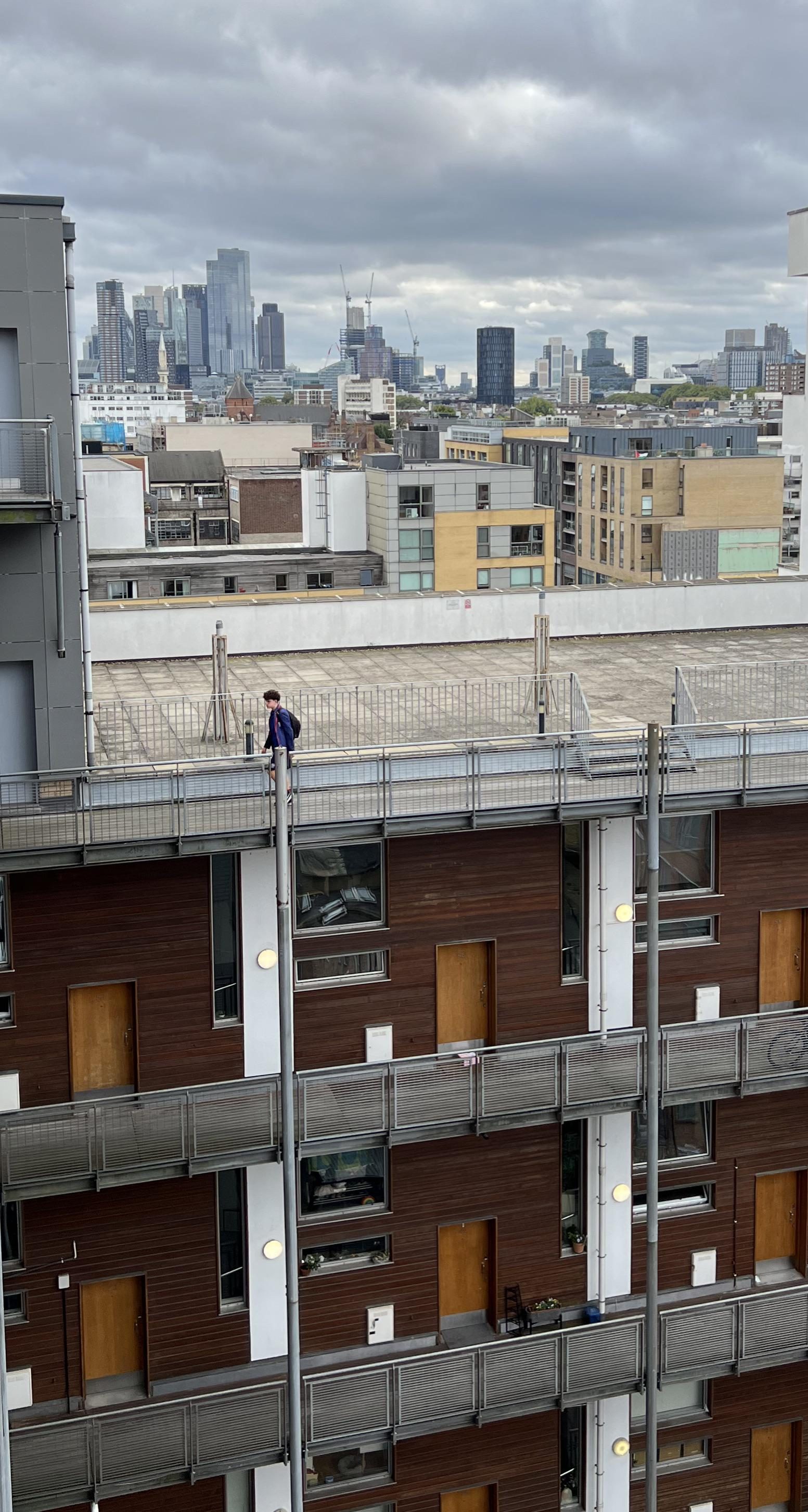 Rooftop walkway at Ability Plaza with the City of London skyline behind, dark cladding enclosing the balconies below