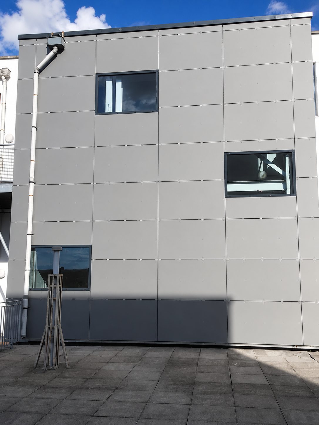 Grey rainscreen cladding panels fitted in a jointed grid across an elevation at Ability Plaza, two windows set within the panels