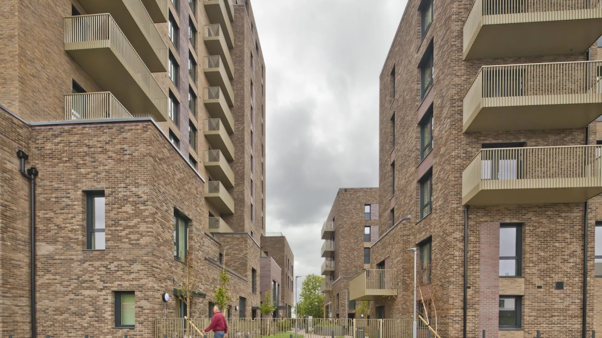Acton Works' brick residential blocks in Park Royal, gold-toned balconies stacked above a landscaped walkway