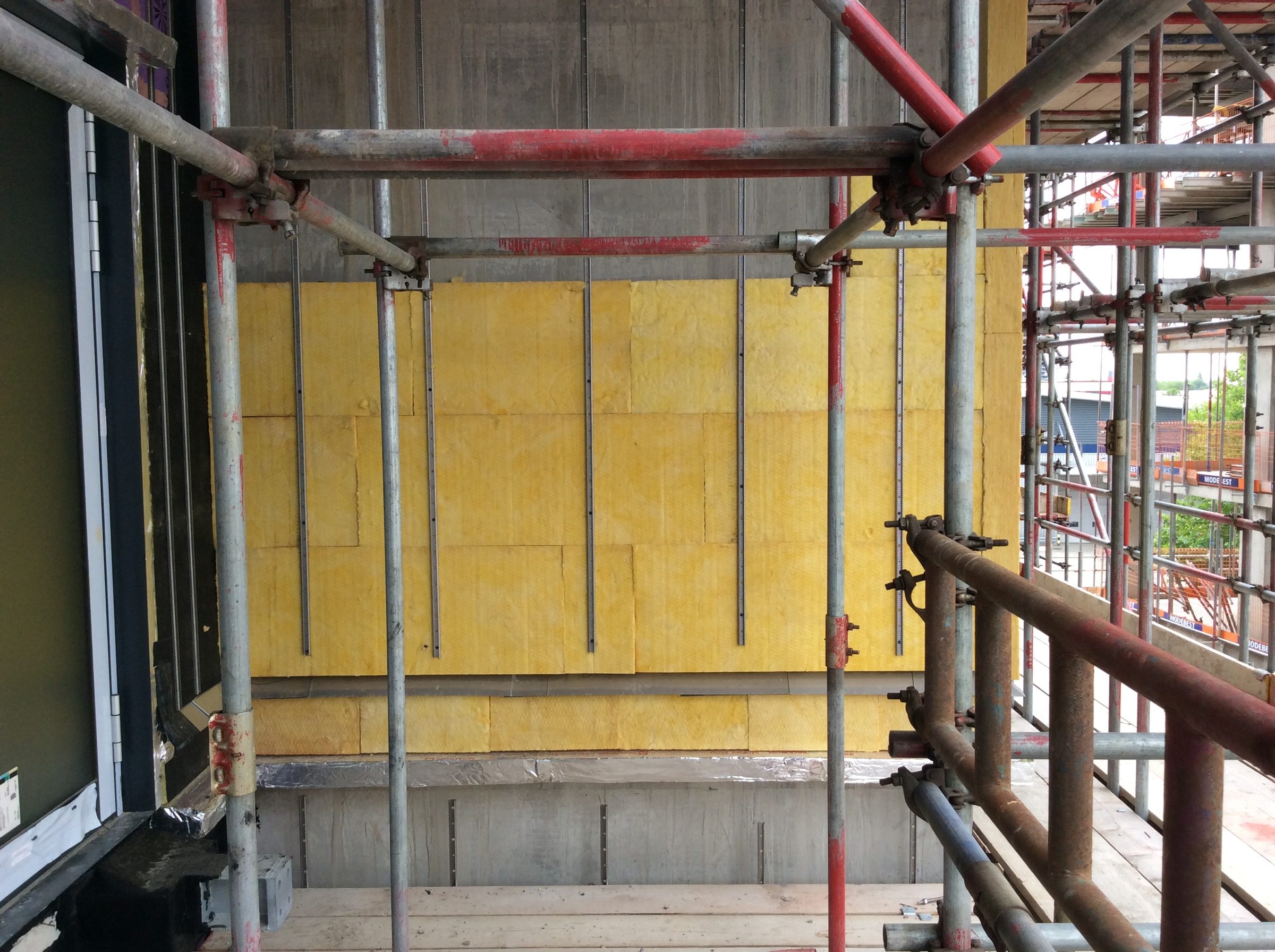 Mineral-wool insulation on an elevation at Acton Works, with rails fixed through it and the scaffold alongside