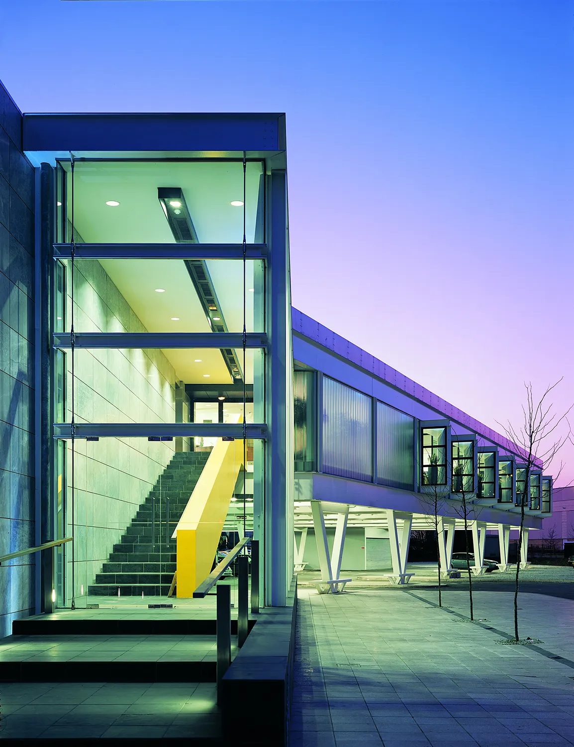 Ashfield House's glazed stair core and the cantilevered white edge of the second-floor pavilion, photographed at dusk