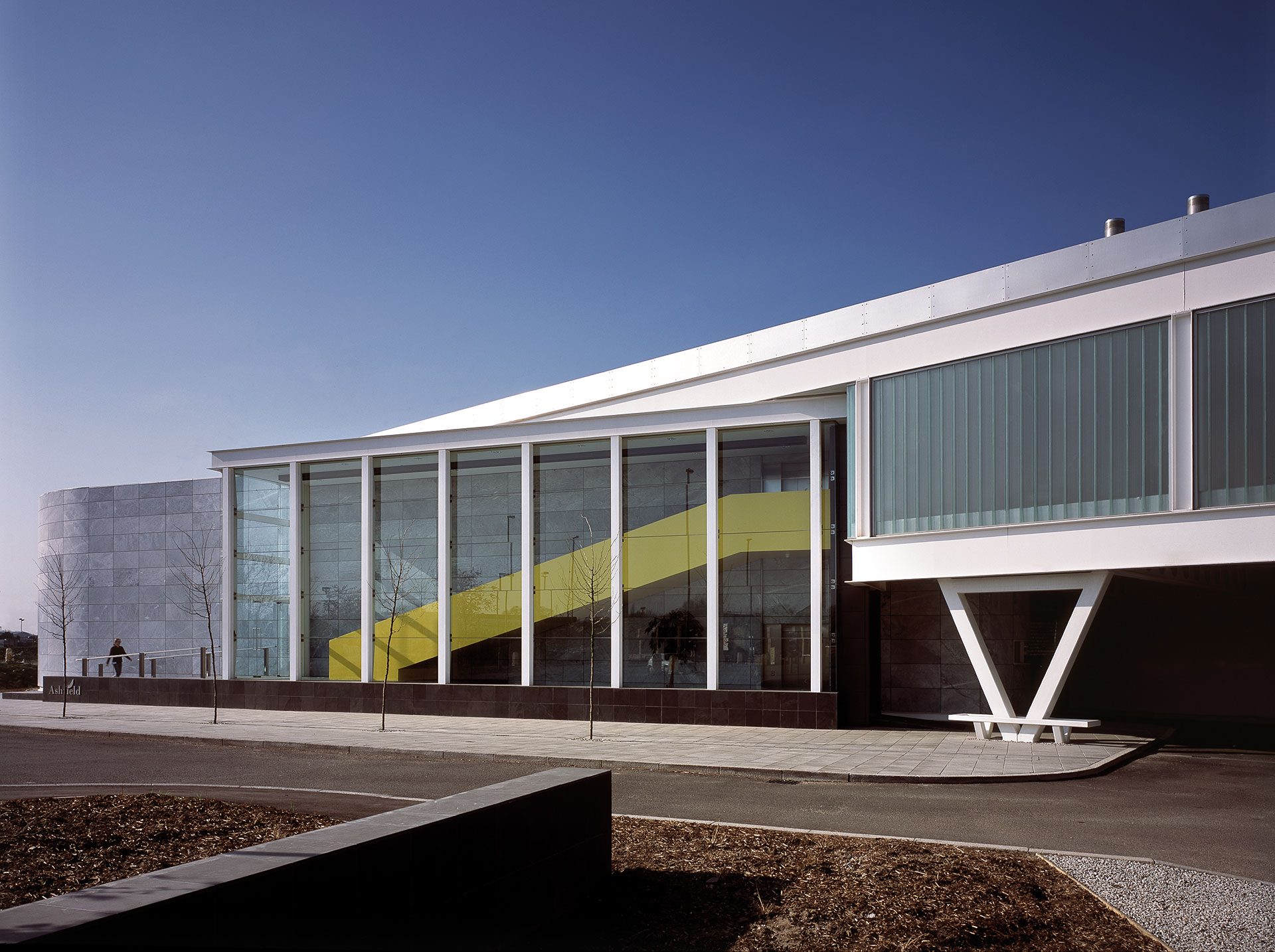 Ashfield House's entrance elevation after the extension, showing the curved stone-clad drum of the original 2002 building beside the glazed atrium stair and the cantilevered pavilion above