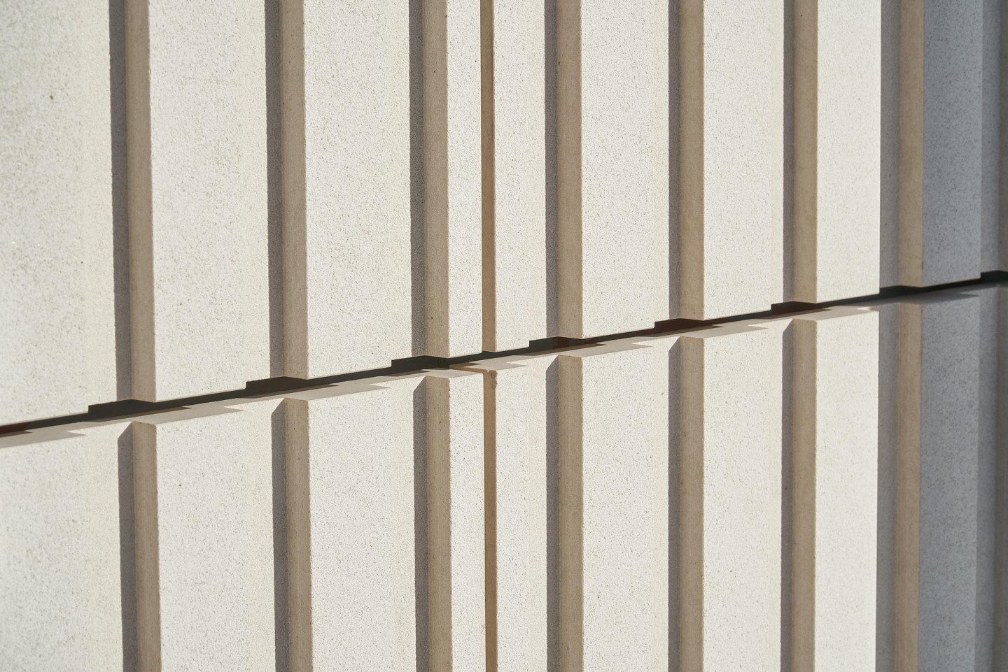 Close-up of cream engineered stone panels with vertical fluting, meeting at a horizontal joint in low sunlight