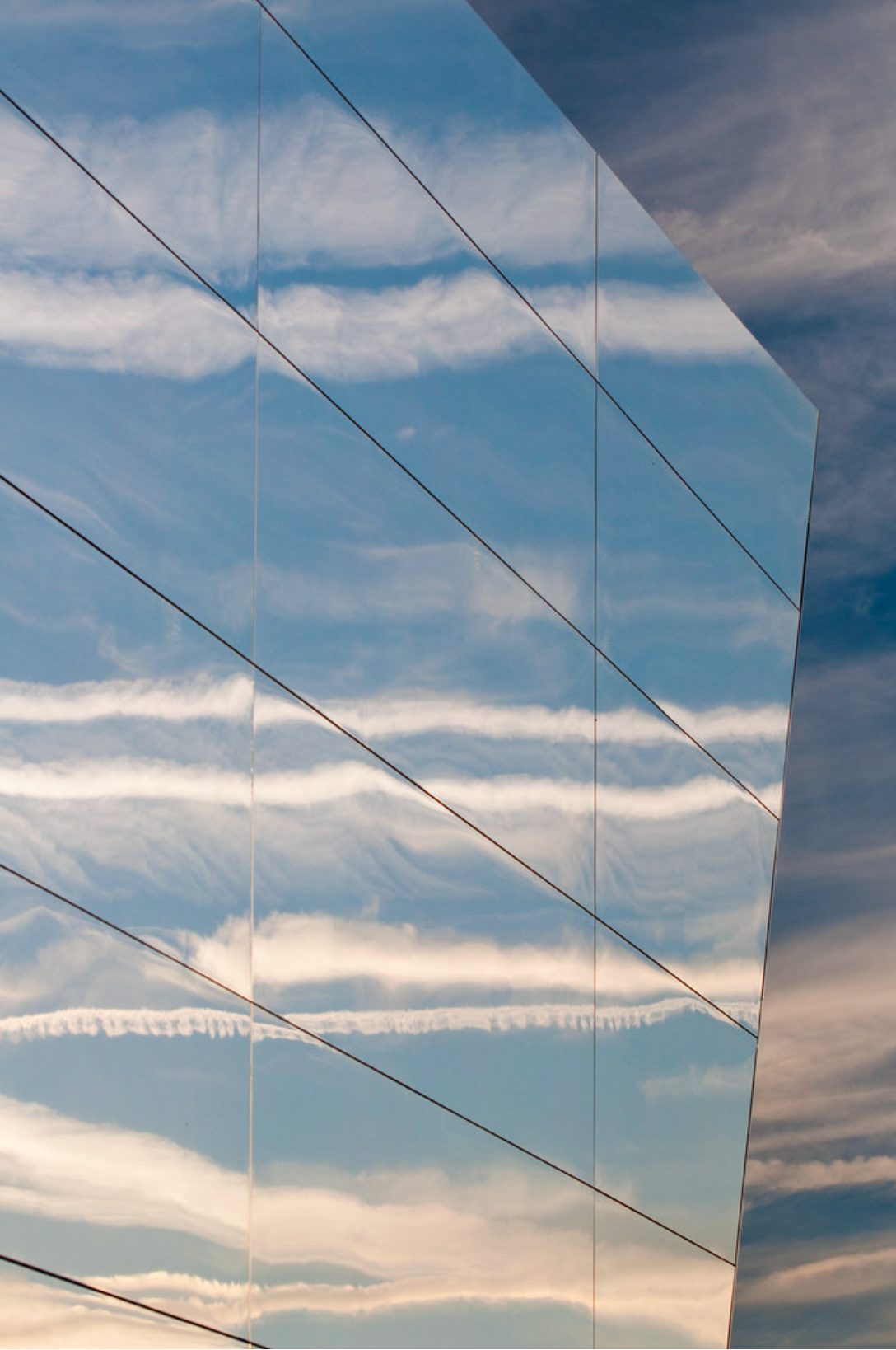 Mirror-finish cladding panels reflecting a blue sky and streaks of cloud on the angled facade of the BP Showcase Pavilion, London 2012 Olympic Park
