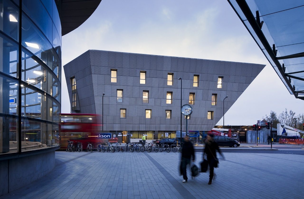 Canada Water Library at dusk seen from the street, with a bus passing and the building's angled form against the sky