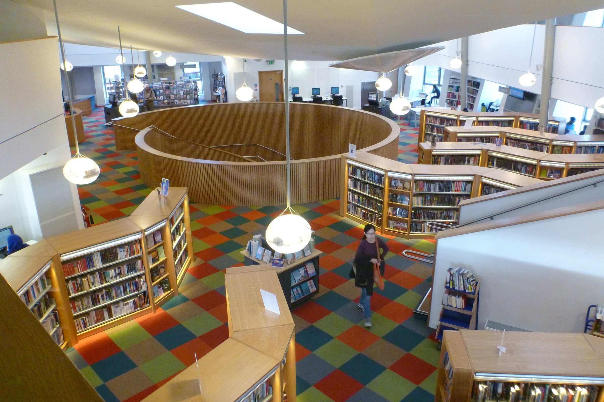 Canada Water Library's main floor viewed from the upper gallery, bookshelves curving around the atrium
