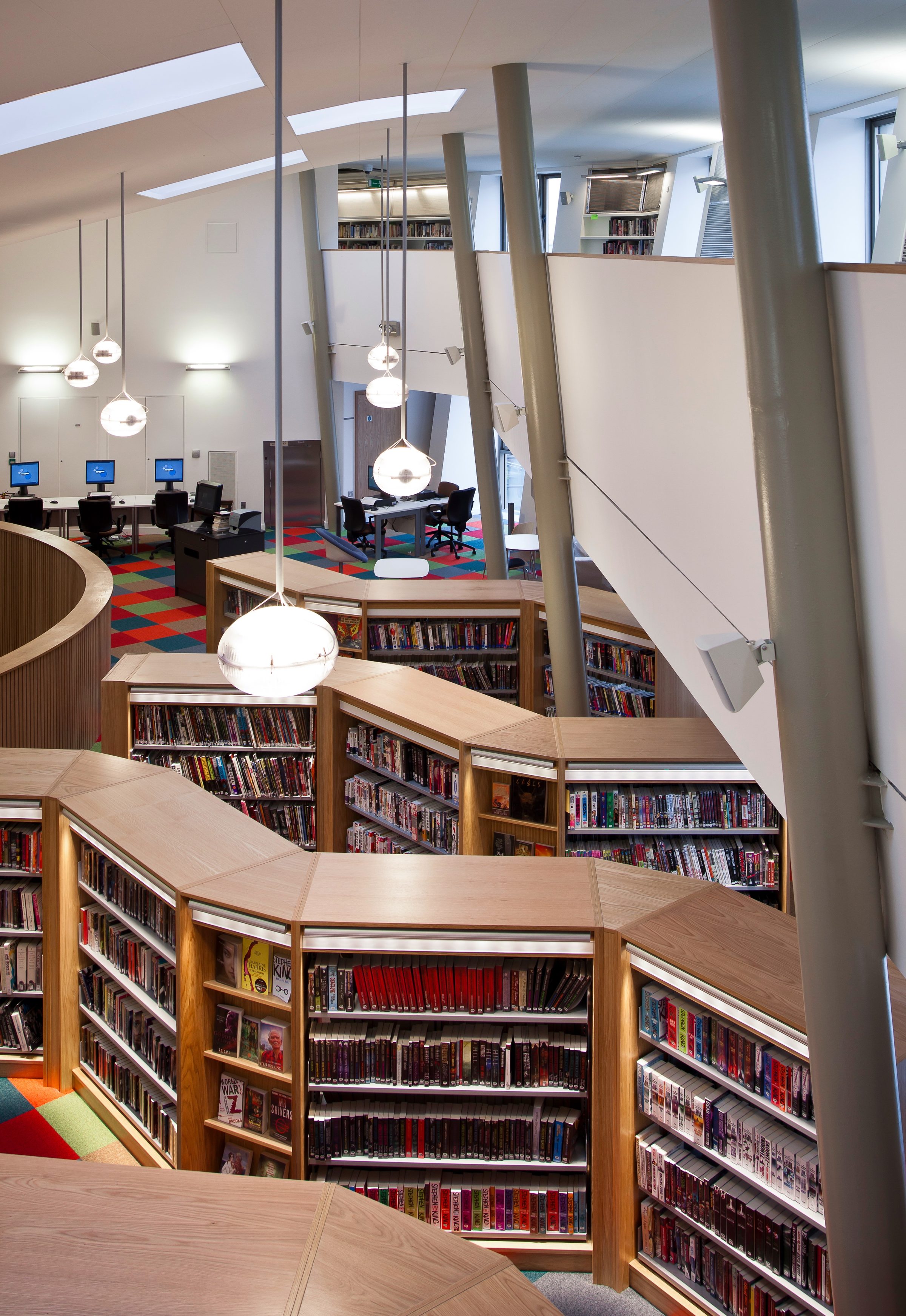 Canada Water Library's upper gallery, bookshelves beneath the raking roof structure and columns