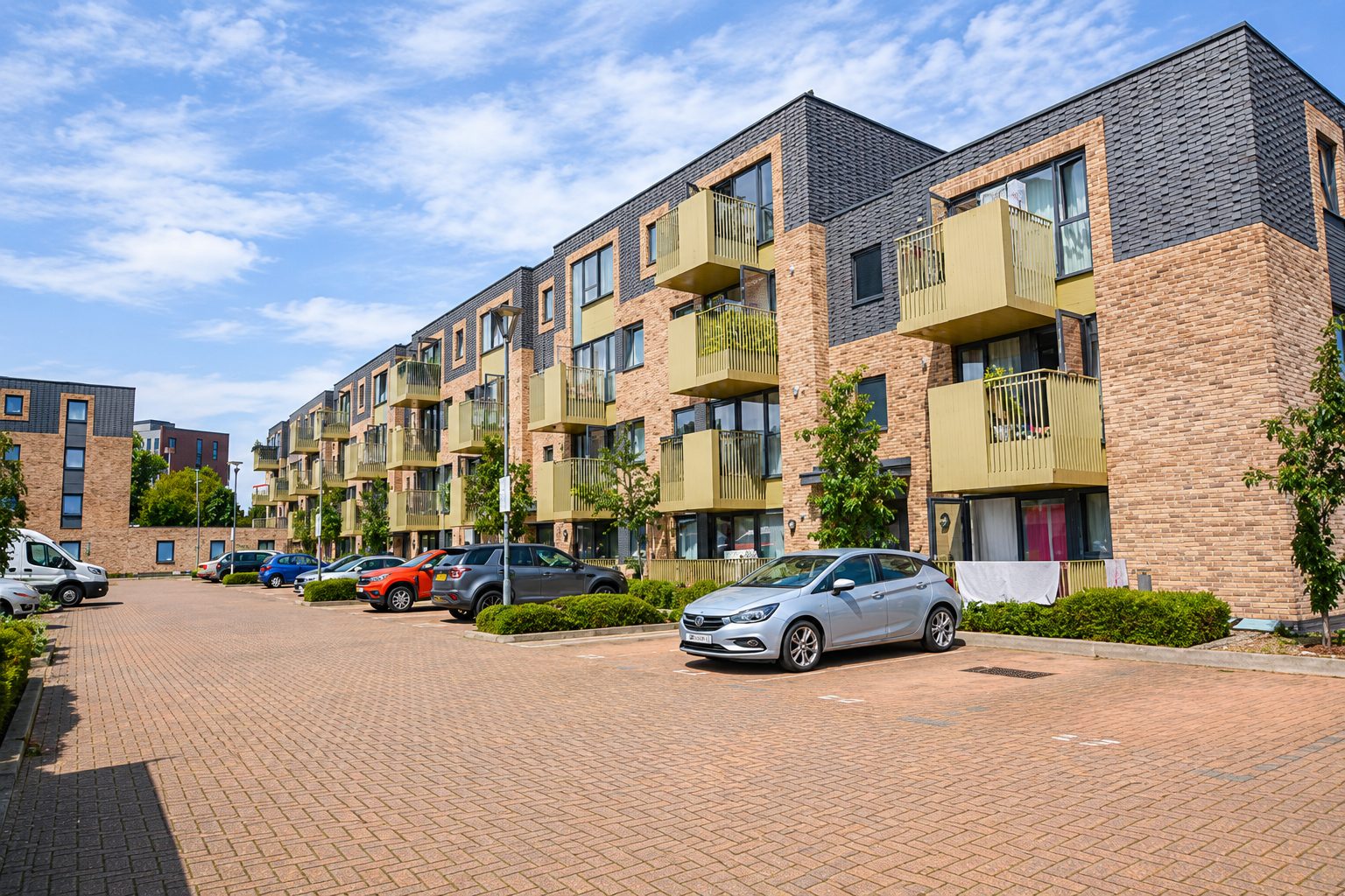 Street-level view of the corner apartment block on Carnarvon Road, brick and dark-tile elevations with pedestrians on the pavement