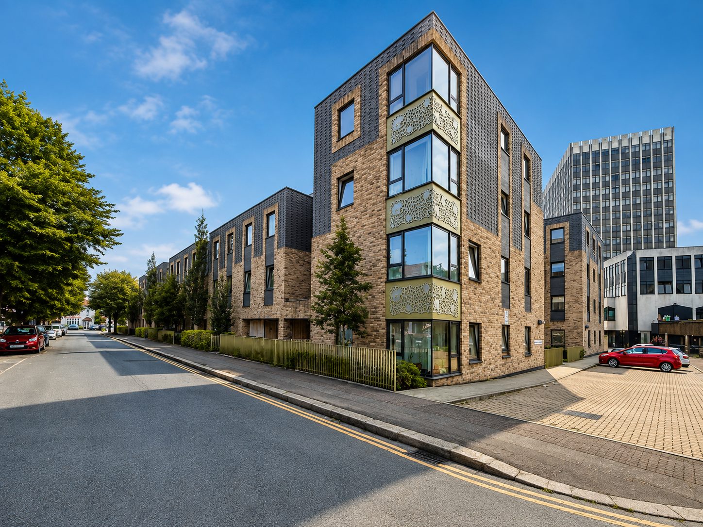 Corner apartment block on Carnarvon Road, brick and dark-tile cladding with a laser-cut decorative panel at the oriel bay, blue sky above
