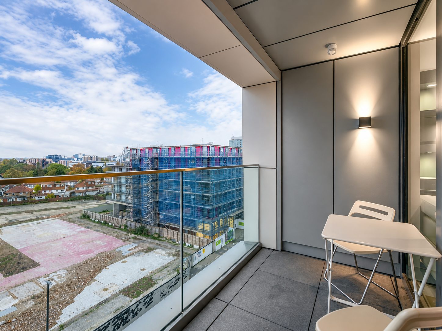 A furnished balcony at Everly House looking out towards a neighbouring building under construction, wrapped in blue netting