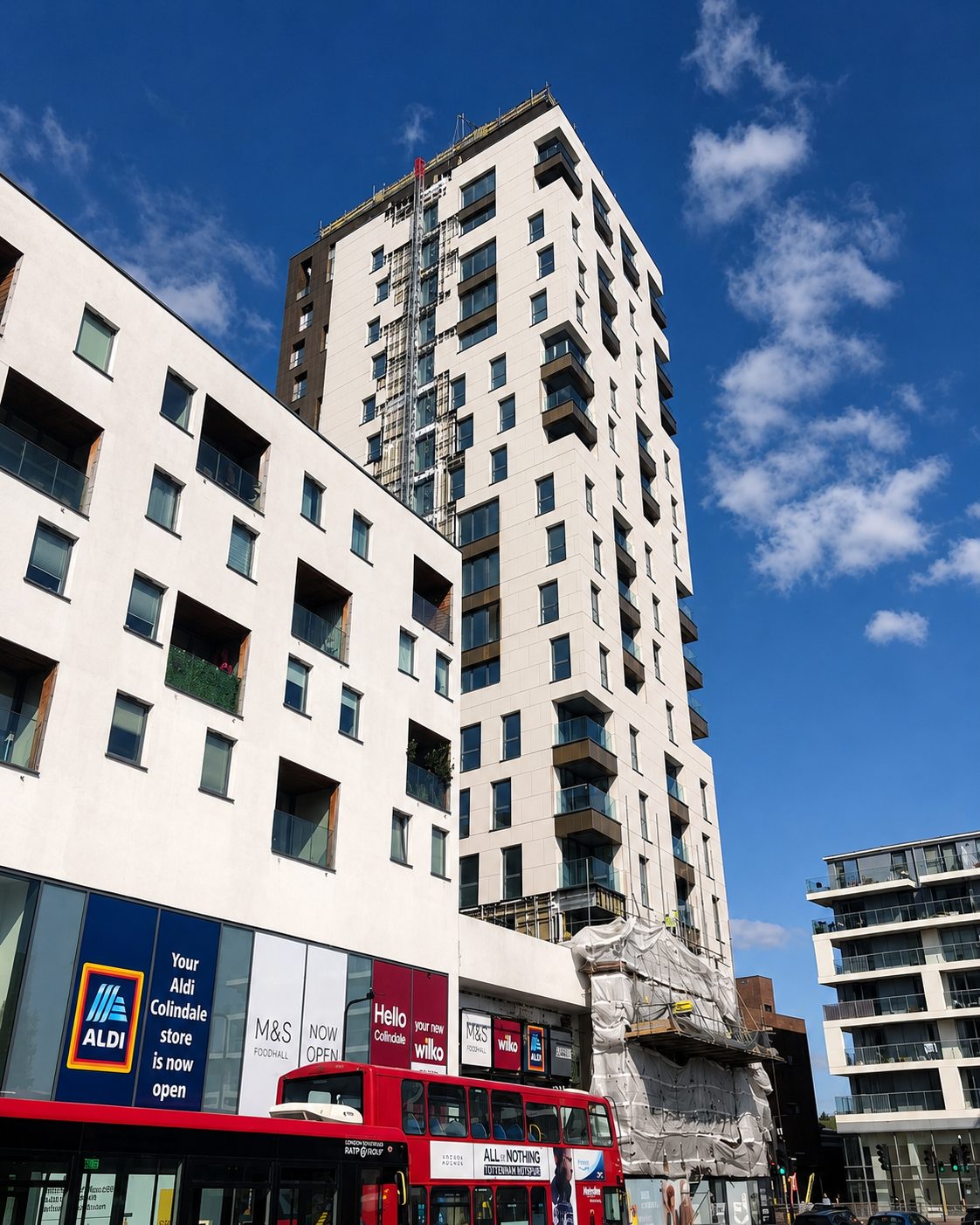 Everly House with scaffold wrap on its lower floors as the façade works near completion, a red bus passing at street level