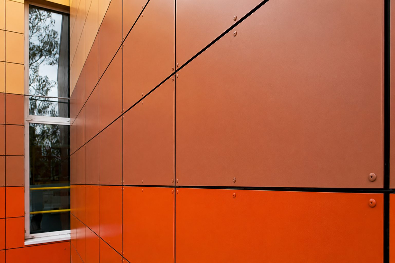 Cladding panels meeting a window reveal at Hawes Down Centre, graded from soft rose to deep orange with visible rivets
