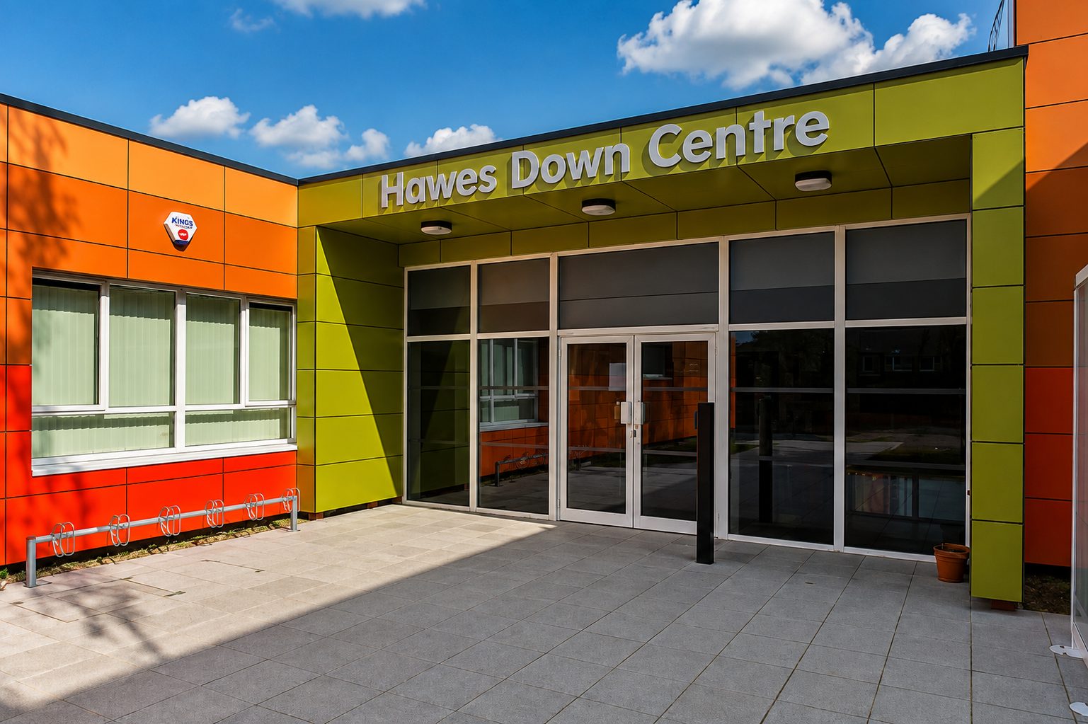 Hawes Down Centre's entrance canopy in olive-green and orange cladding panels, with the building's name above the glazed doors