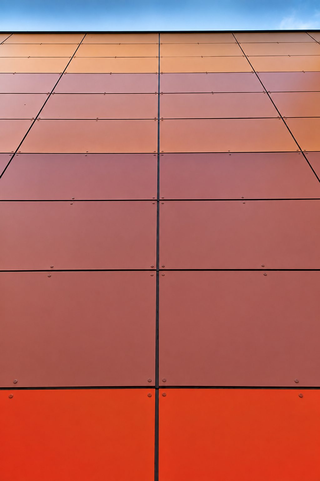 Close view of the graded amber-to-red multicoloured cladding panels at Hawes Down Centre, with expressed dark joints and mechanical face fixings
