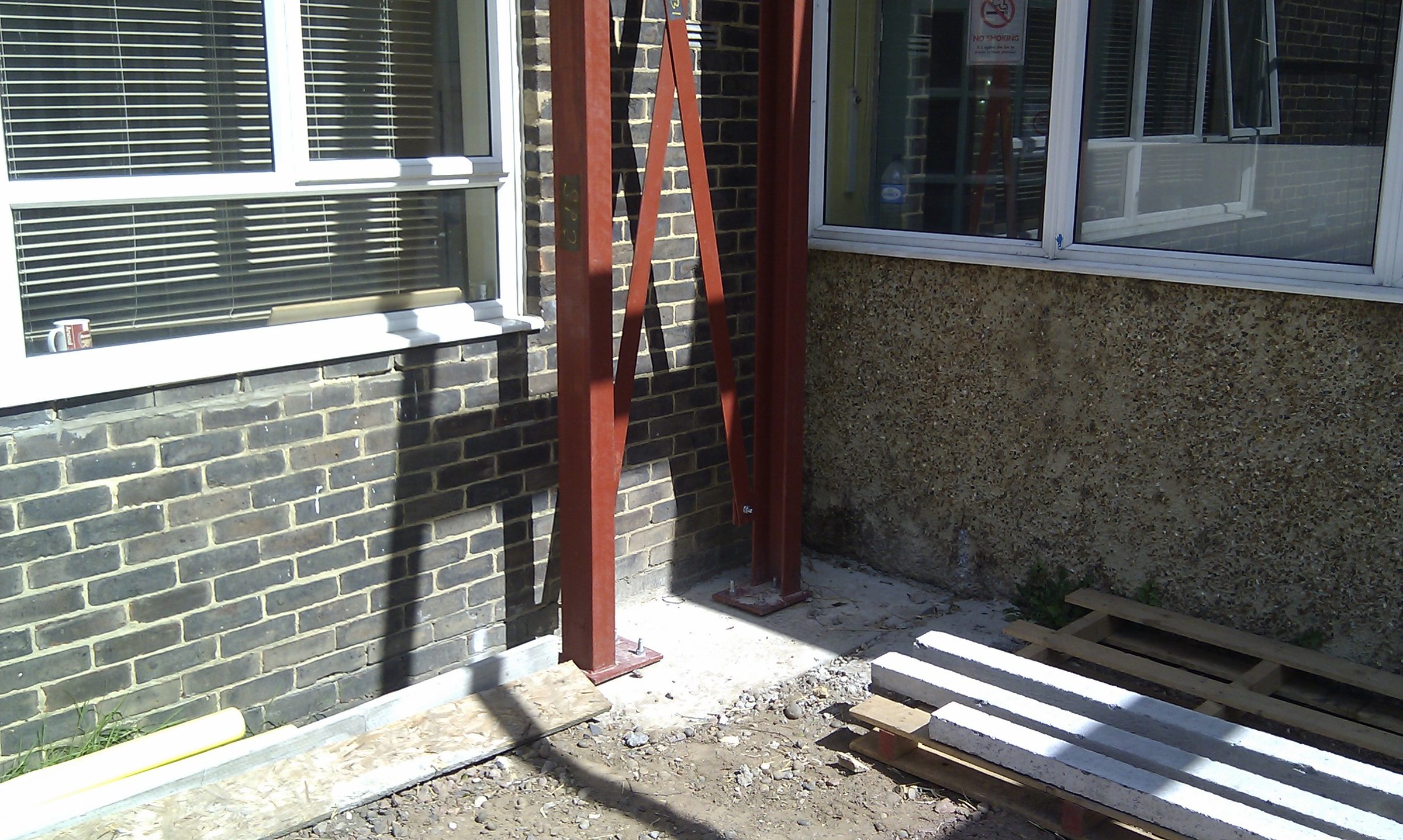 Steel column and diagonal cross-bracing on a base plate beside the existing brick elevation at Hawes Down Centre