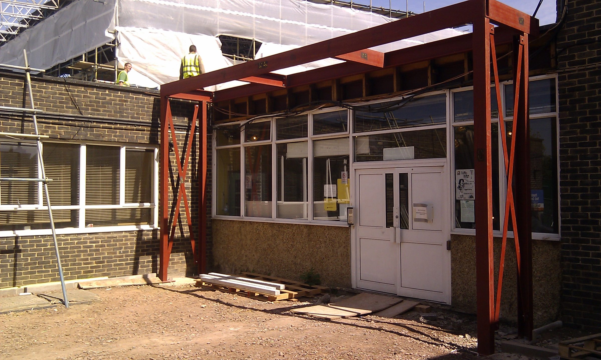Red-oxide primed steel frame and canopy structure erected against the existing brick elevation at Hawes Down Centre during the 2011 refurbishment