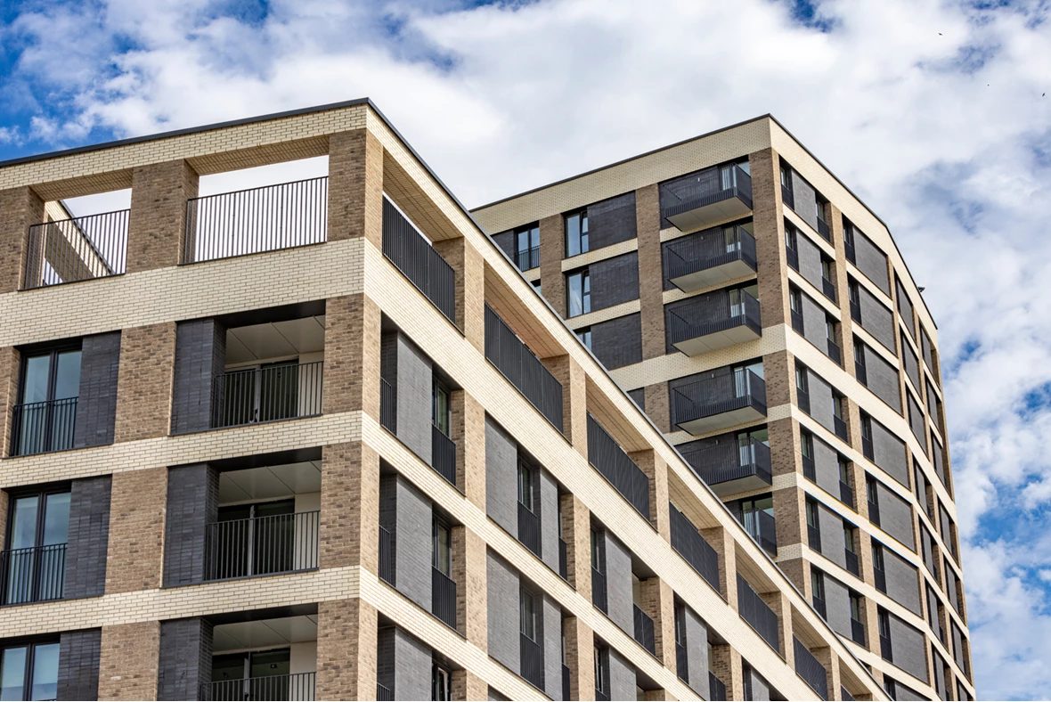 Upper storeys of Plaistow Hub's two residential blocks, buff brick frames around dark grey panels and balconies