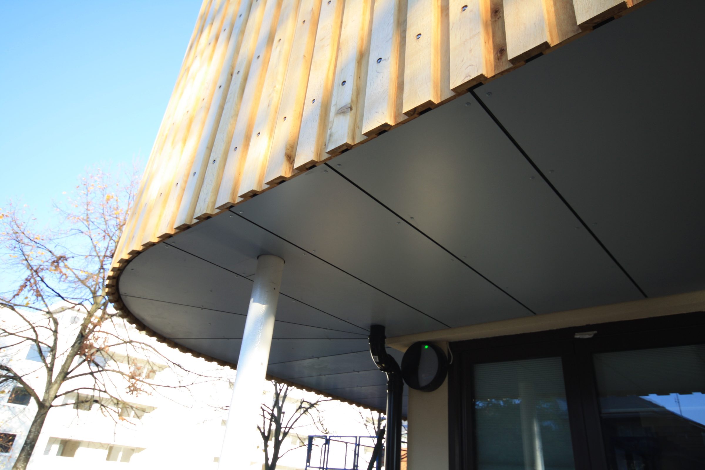 Corner of the curved canopy soffit at Putney High School, with timber battens and a rainwater outlet