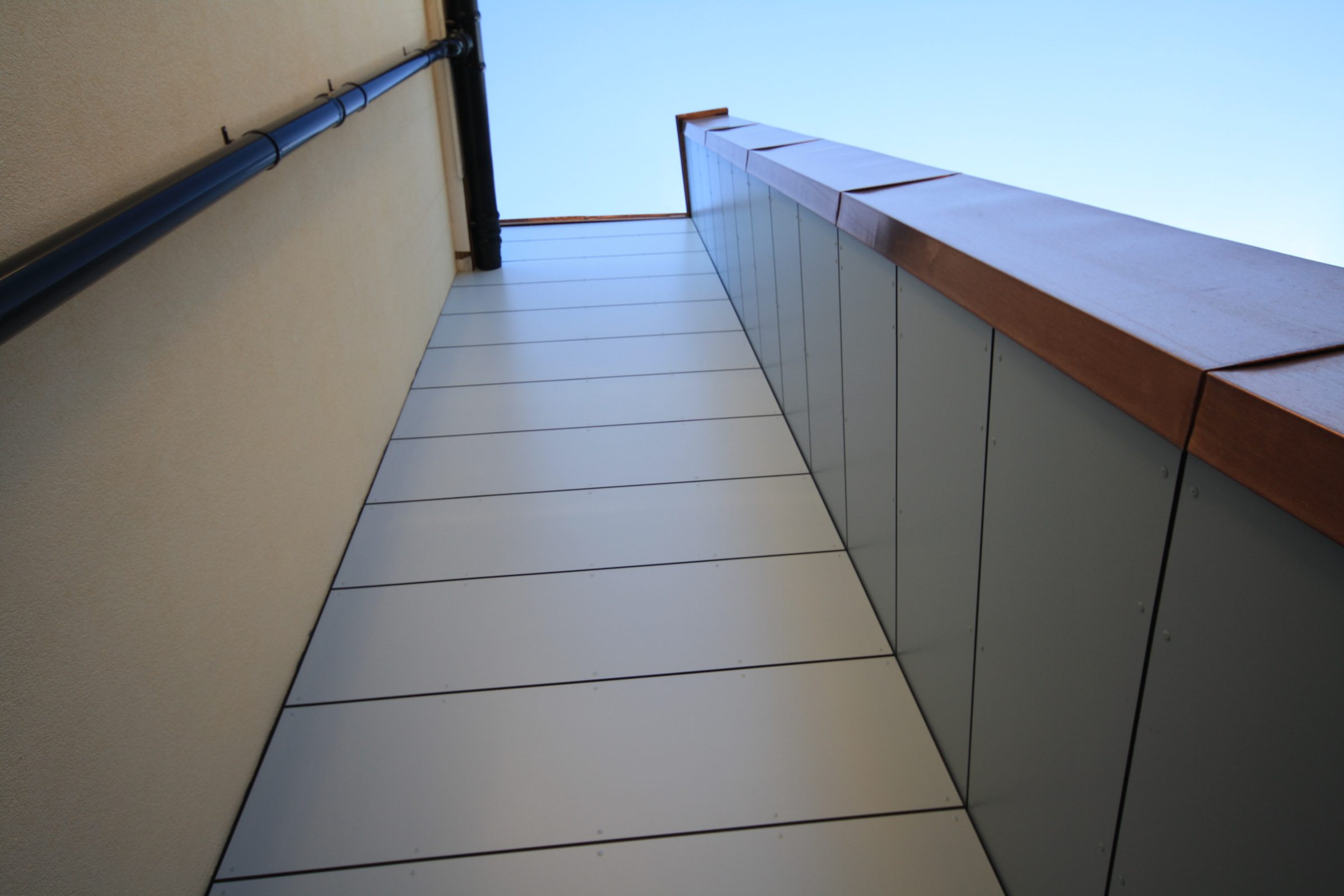 Grey panelled soffit meeting a copper-capped parapet along an elevated walkway at Putney High School