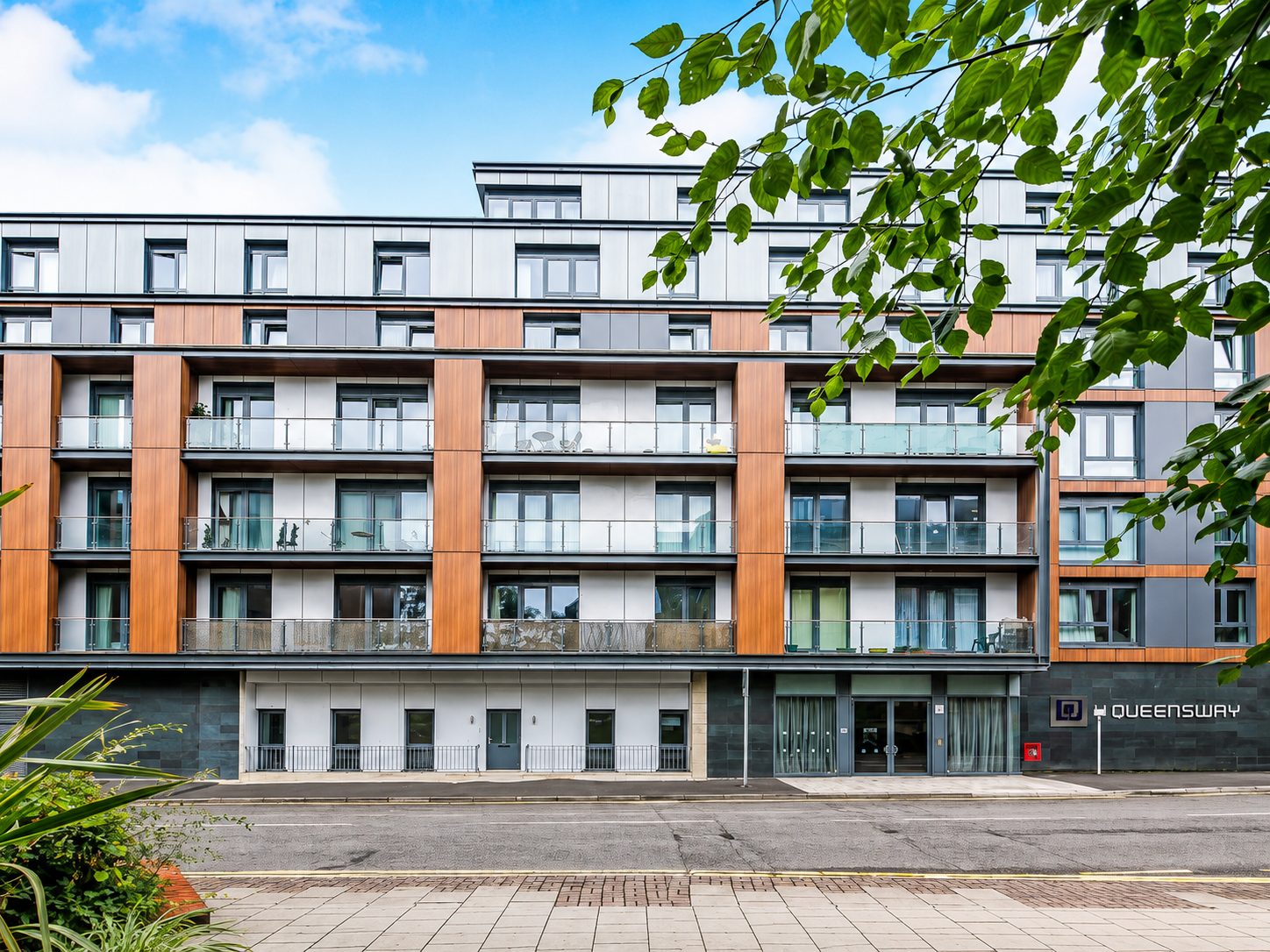 Balcony elevation and 'Queensway' entrance signage at Nobel House, Redhill, framed by tree branches