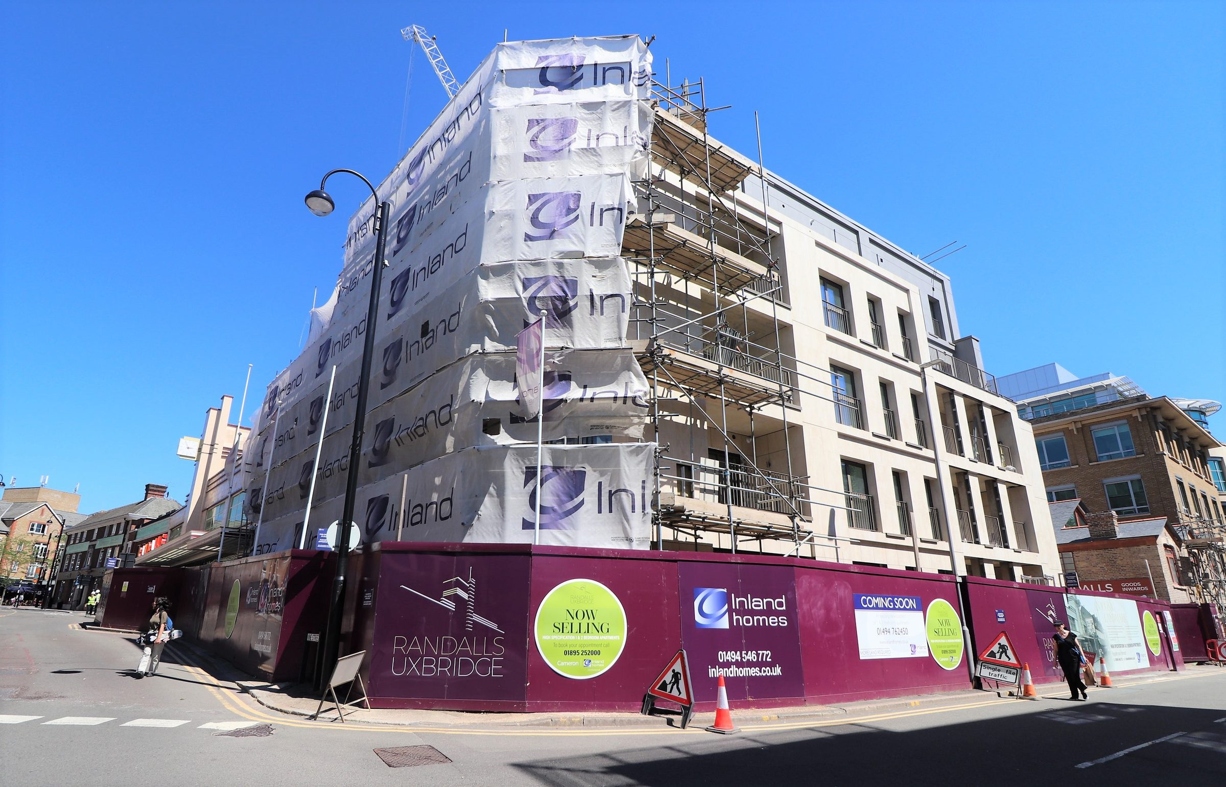 The Randall's Uxbridge site mid-construction, hoarding and scaffold-netting at street level with ceramic granite panels fixed above