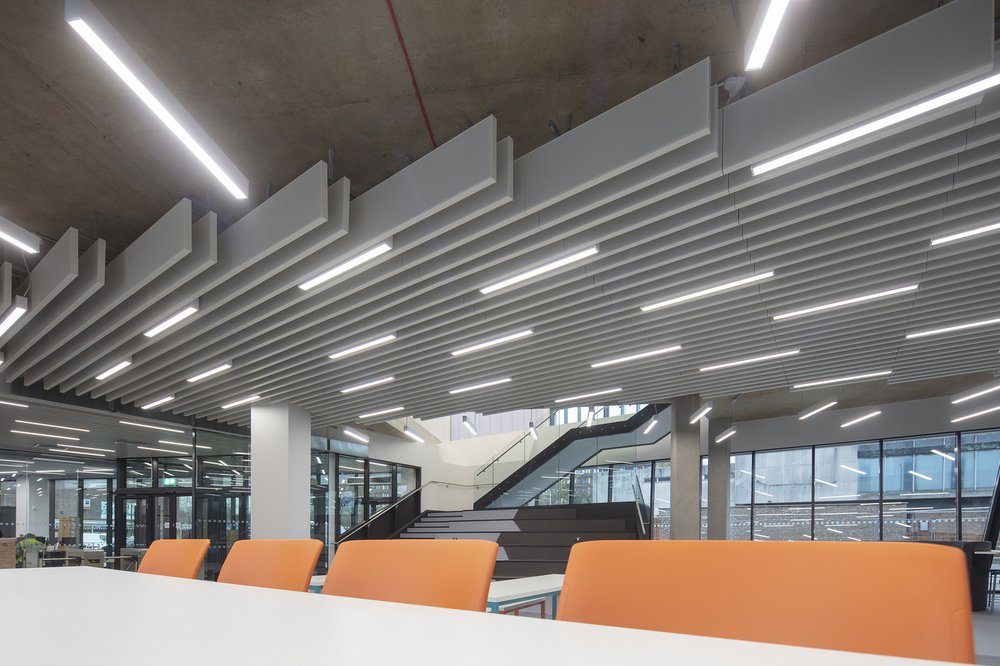 Acoustic ceiling baffles and orange breakout seating inside the Centre for Digital Technologies, overlooking the atrium stair