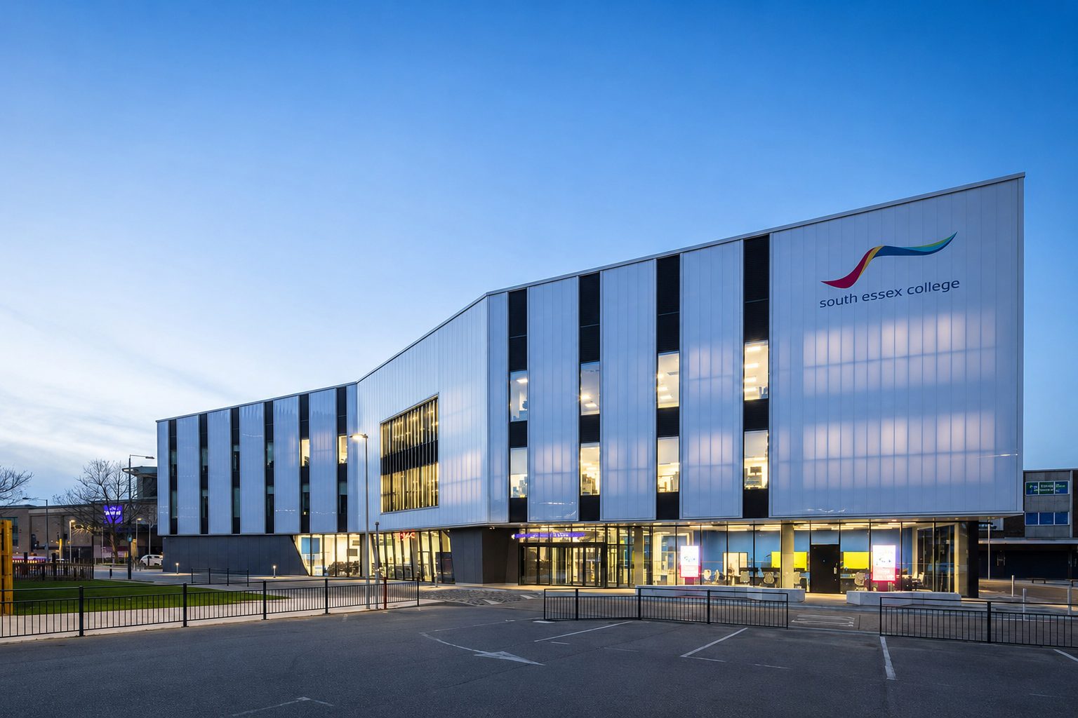 The Centre for Digital Technologies' full elevation at dusk, south essex college signage lit above the forecourt railings
