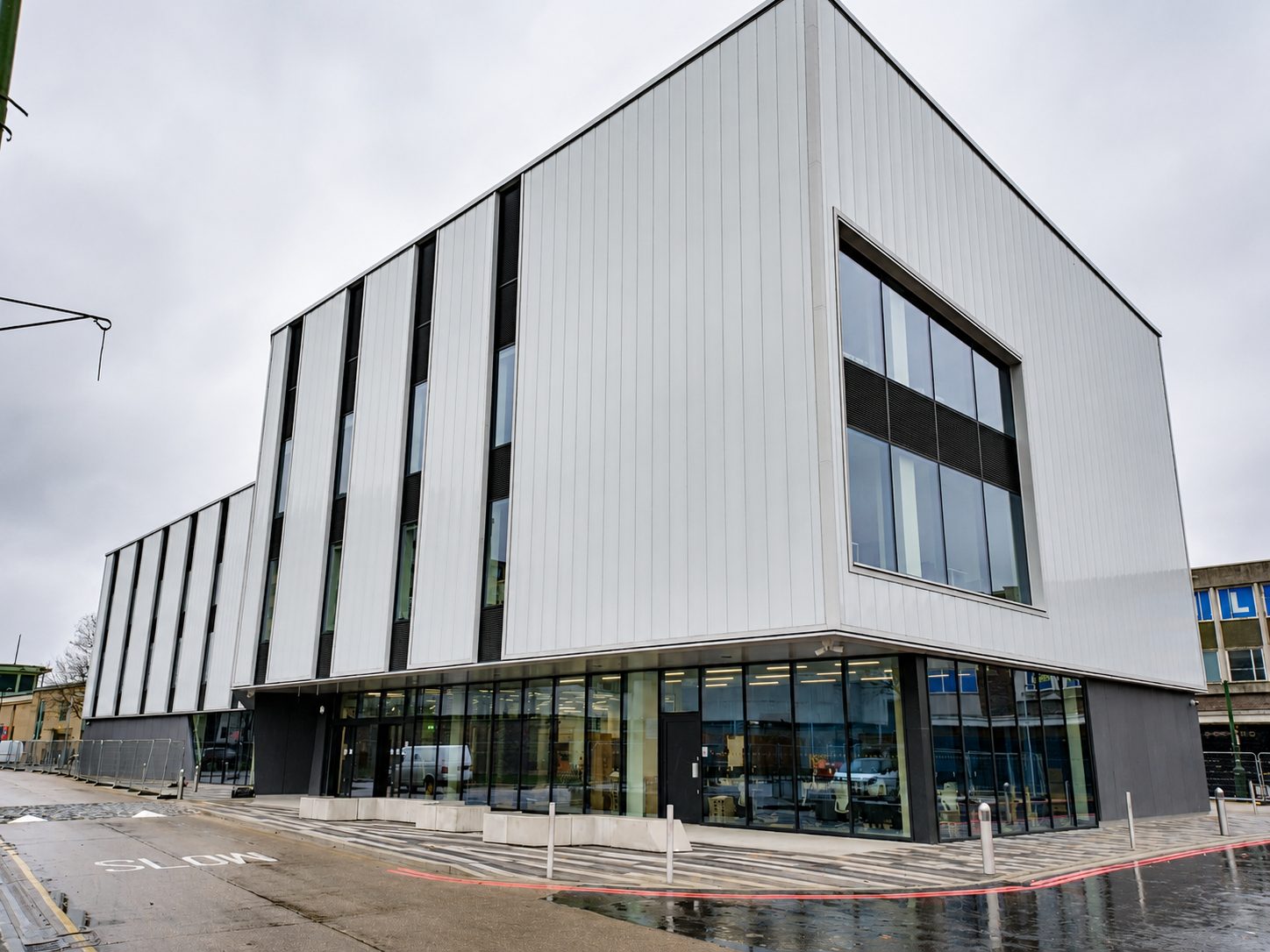 The Centre for Digital Technologies on a wet, overcast morning, its ground-floor glazing lit and a road marked SLOW in the foreground