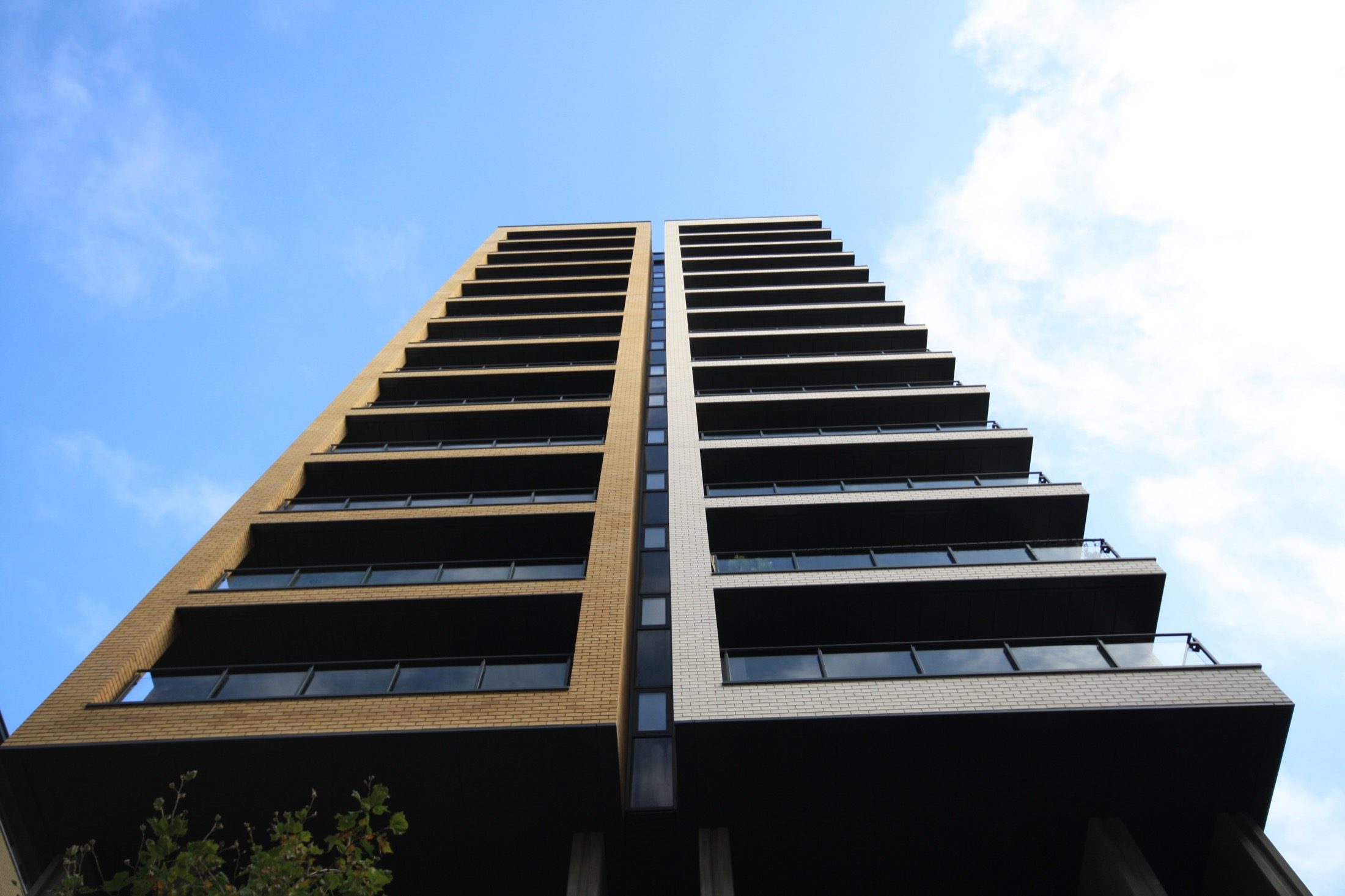 Looking up a Suttons Wharf North tower: dark panelled balcony fronts and soffits framed by buff and white brick, Bethnal Green