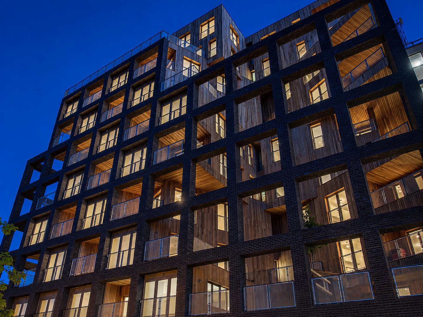 The Cube's ten-storey elevation lit at dusk, every balcony and window glowing, in its original cedar-clad form