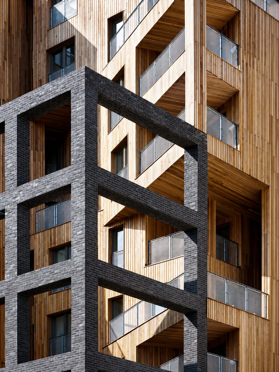 Close view of The Cube's black-brick portal frame holding cedar-clad balcony volumes at an angle