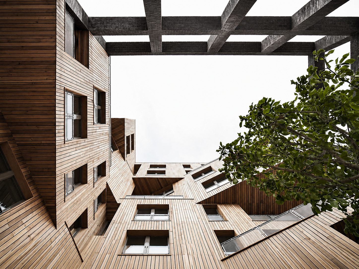 Upward view through The Cube's courtyard opening, the black-brick portal frame crossing overhead against a hazy sky