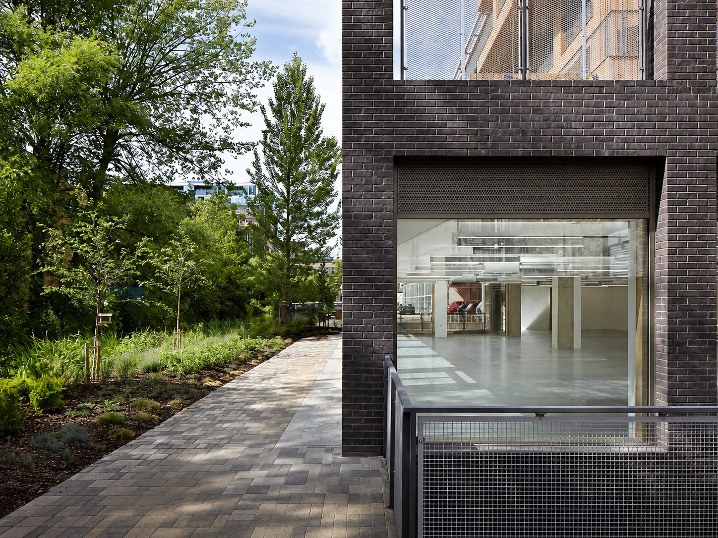 The Cube's black-brick ground floor and glazed undercroft, beside a landscaped path on Wenlock Road