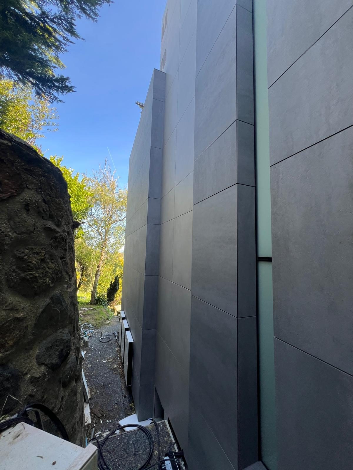 Close view of the light-channel gap between charcoal and pale grey engineered stone panel runs at The Lighthouse, with ventilation grilles set into the reveal