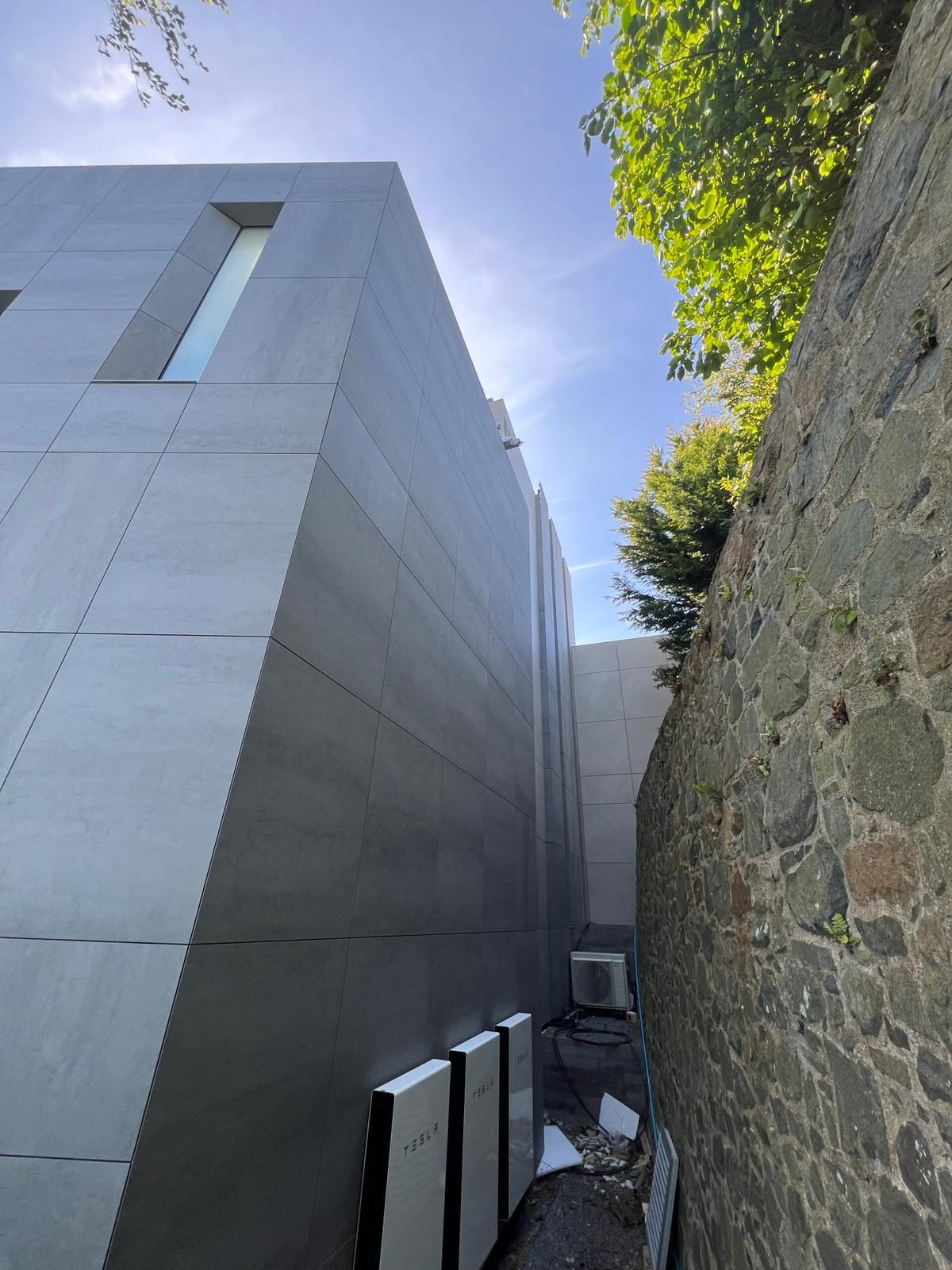 The Lighthouse's south corner, where pale and dark engineered stone panel runs meet a mitred edge above Fort George's original stone boundary wall