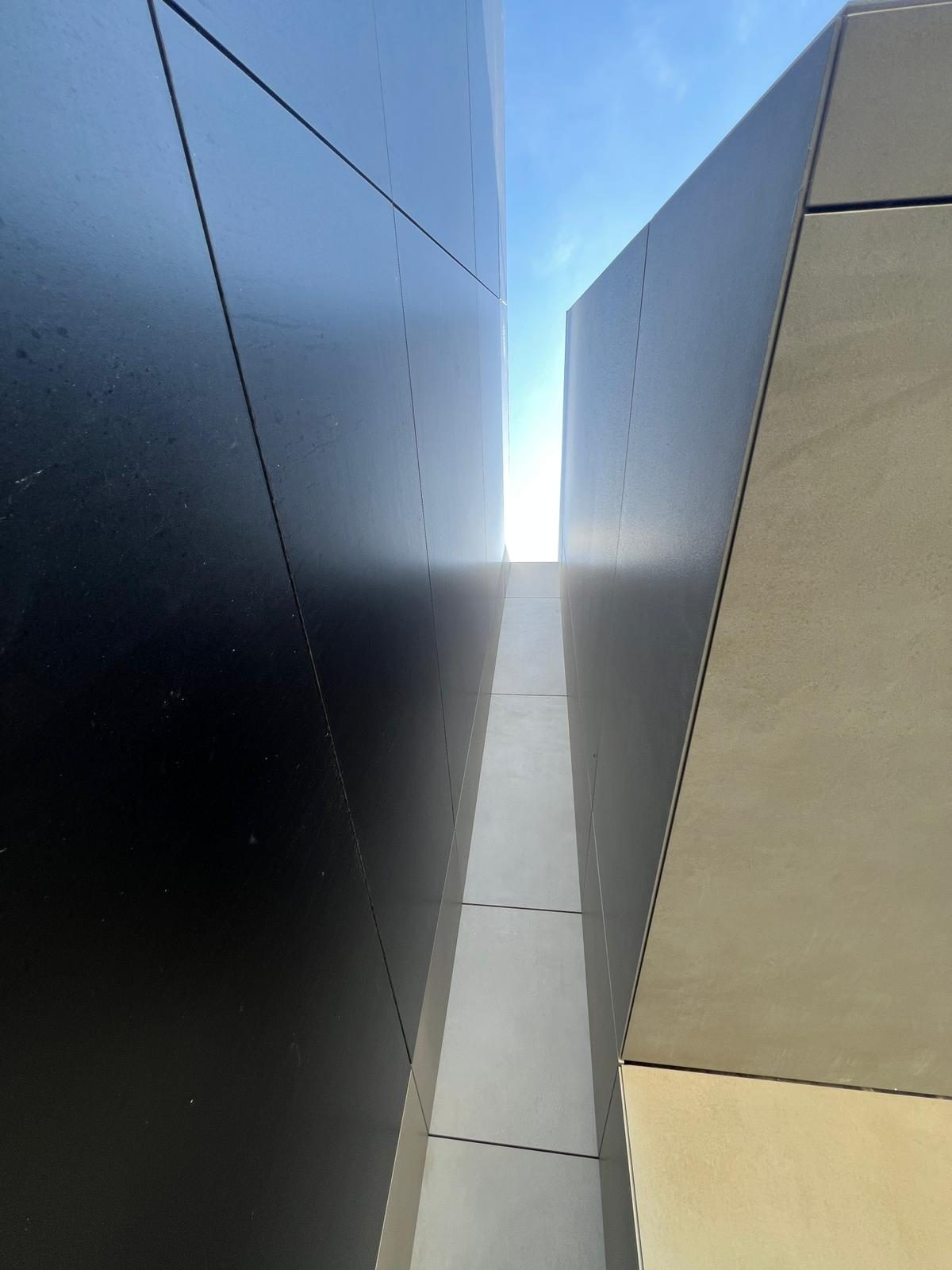 Looking straight up a narrow light-channel gap between a black panel volume and a grey engineered stone panel volume at The Lighthouse