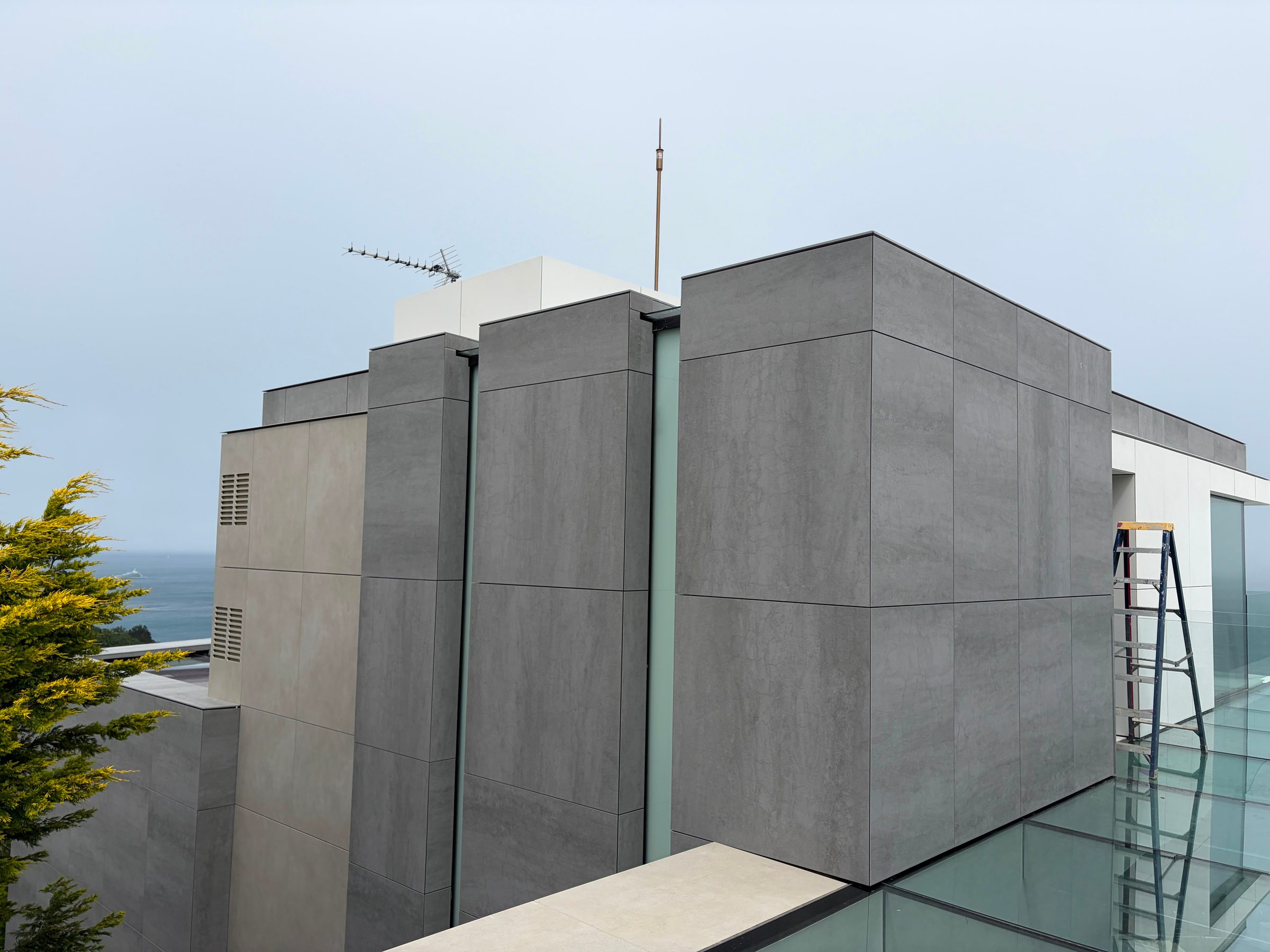 Close view of grey engineered stone panels cladding a roof-level plant enclosure at The Lighthouse, with the sea visible in the distance