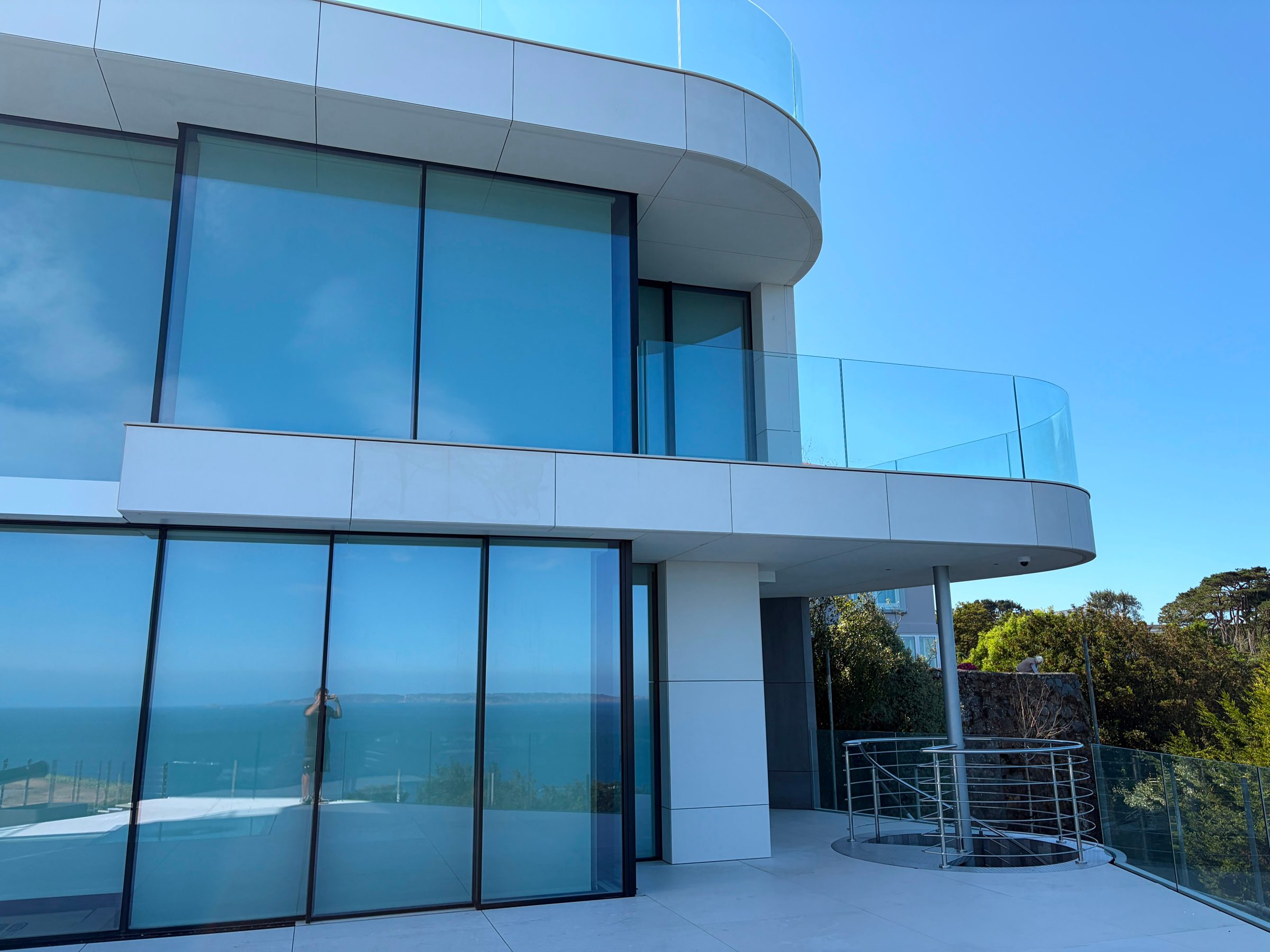 Close view of The Lighthouse's curved glazed balcony structure above a spiral stair down to the lower terrace, with the sea beyond