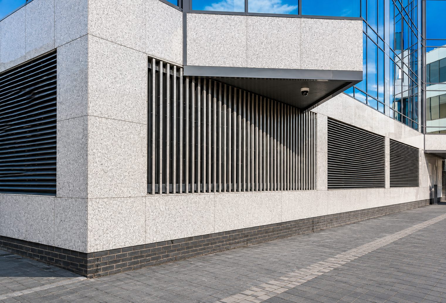 Large pale speckled granite panels set out around dark louvre openings beneath a projecting soffit