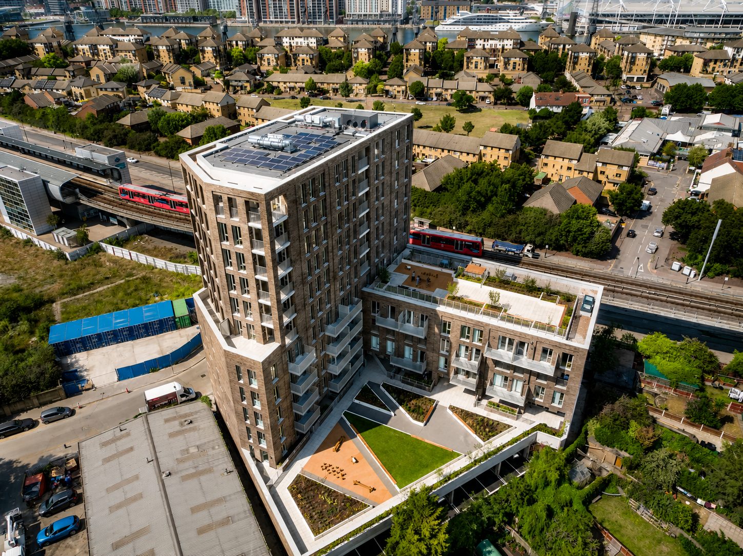 Aerial view of The Refinery’s brick tower with rooftop solar panels, beside a lower block with a landscaped roof garden