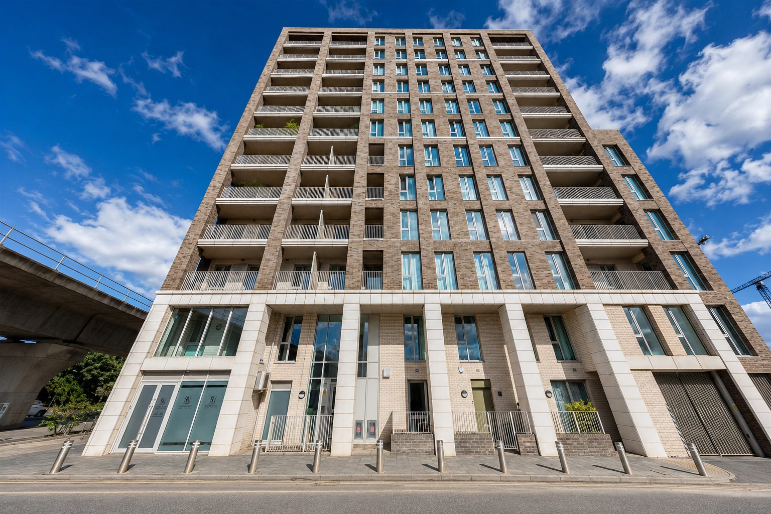 Street-level view of The Refinery’s brick and stone tower base, with ground-floor commercial units and steel bollards