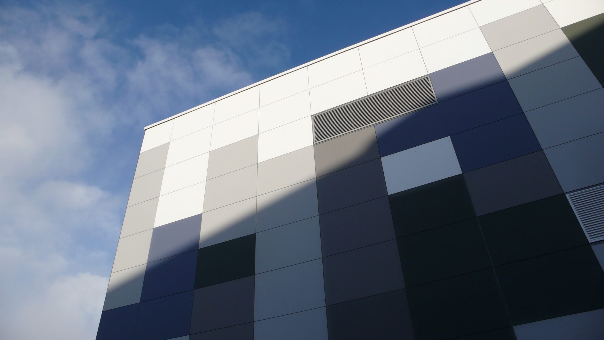 Close view of graduated grey Eternit Pictura fibre-cement cladding panels rising to the corner of a building at Vodafone's Swindon data centre, blue sky behind