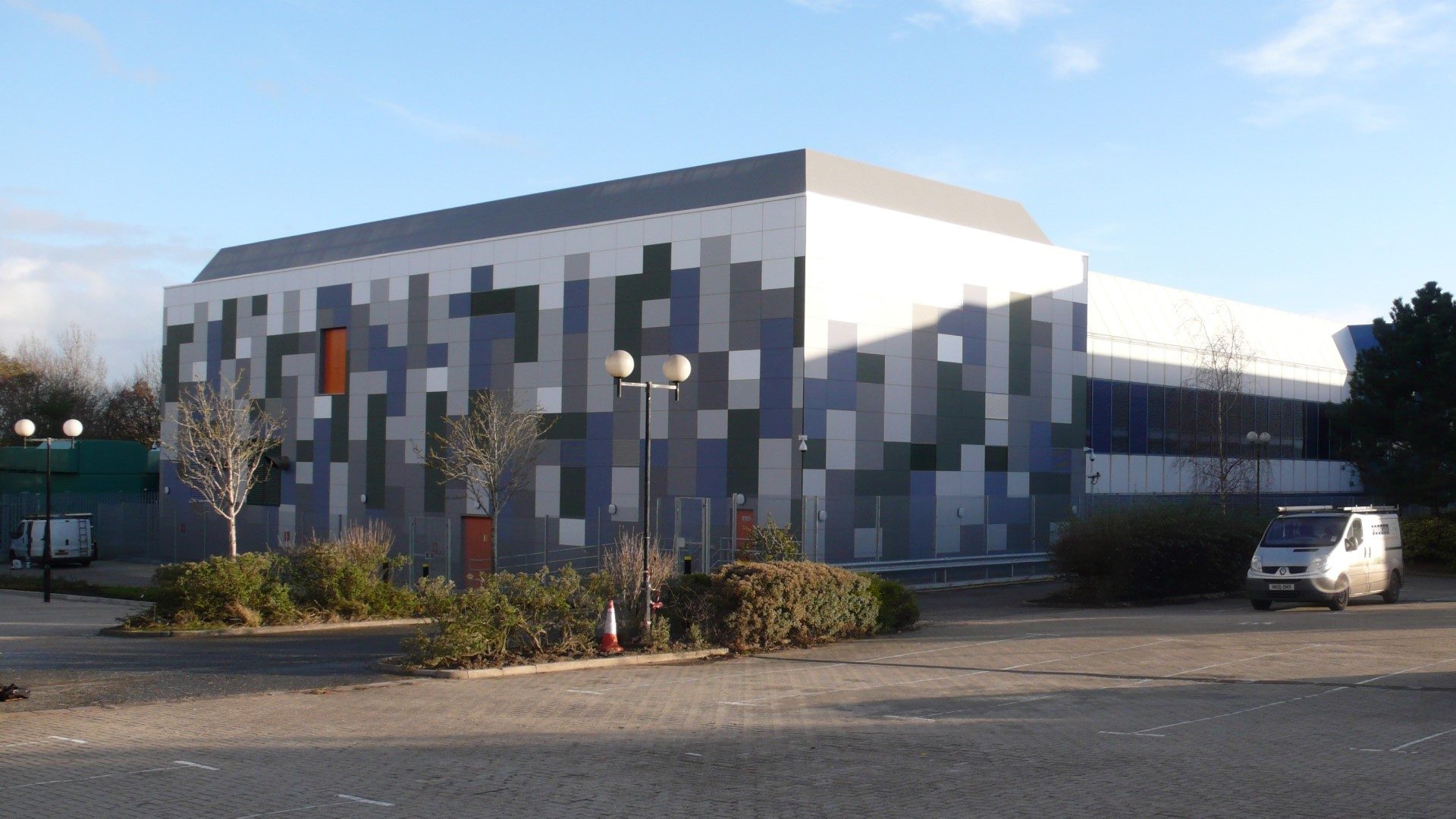 Wide view of a building at Vodafone's Swindon data centre clad in graduated blue-grey, green and pale Eternit Pictura fibre-cement panels, with an orange door and security fencing in front